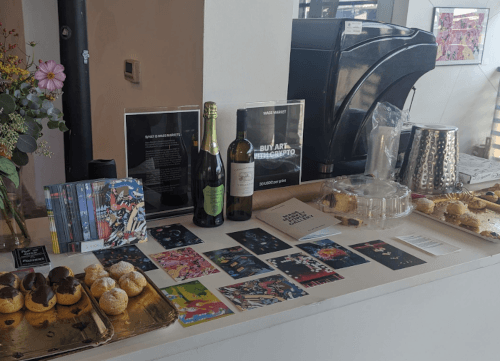 Our stall at EthRome: a table dressed with an array of postcards, two bottles of wine and a sign that says 'buy art with crypto' 