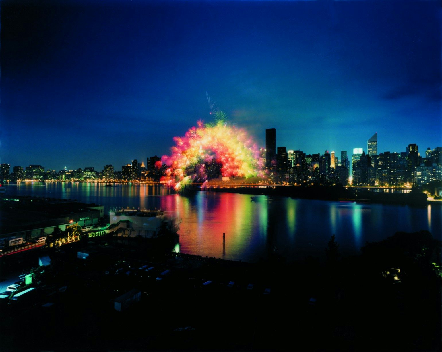 蔡国强，《移动彩虹》，2002。于纽约的东河上实施、从曼哈顿到皇后区，纽约， 6月29日，晚上9:30分, 历时15秒钟。1000枚3英吋大小、安装了电脑芯片的彩色牡丹花型焰火，爆破半径约200米